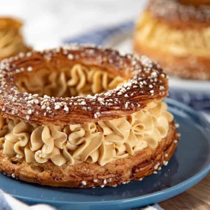 Paris brest pastry on a blue plate filled with praline mousseline cream and topped with pearl sugar.