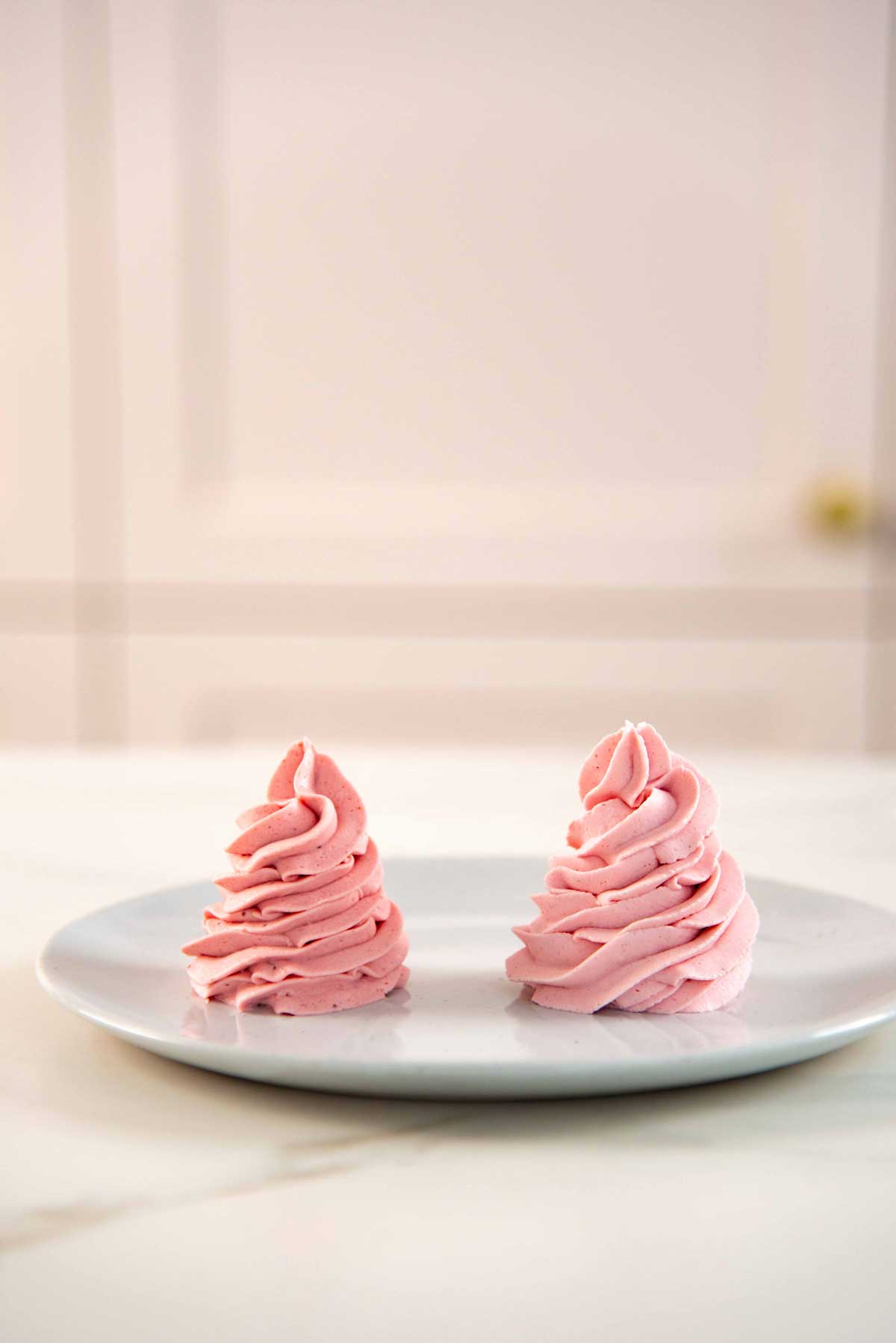 Two large swirls of pink strawberry whipped cream on a small white plate.