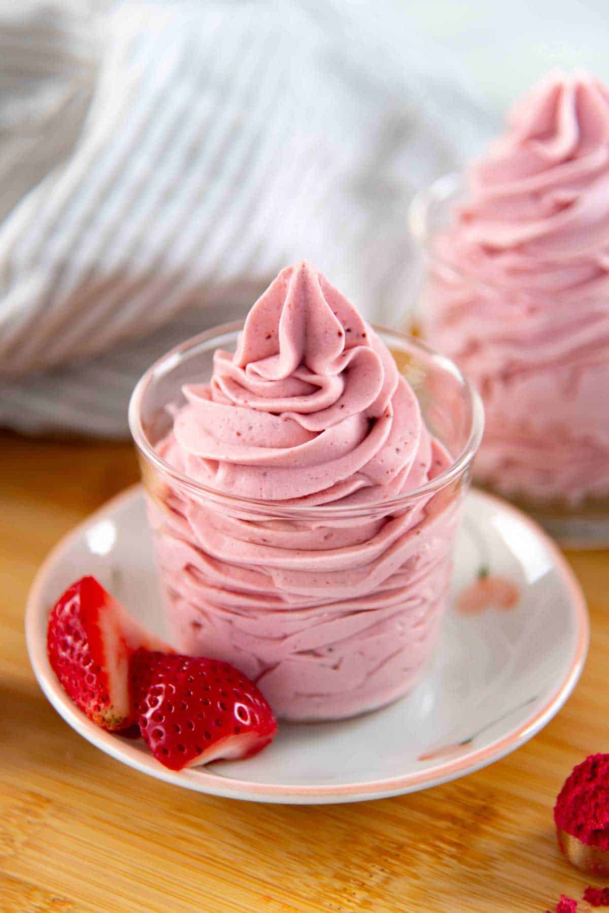 A small glass cup filled with swirled strawberry whipped cream and a sliced fresh strawberry next to it.