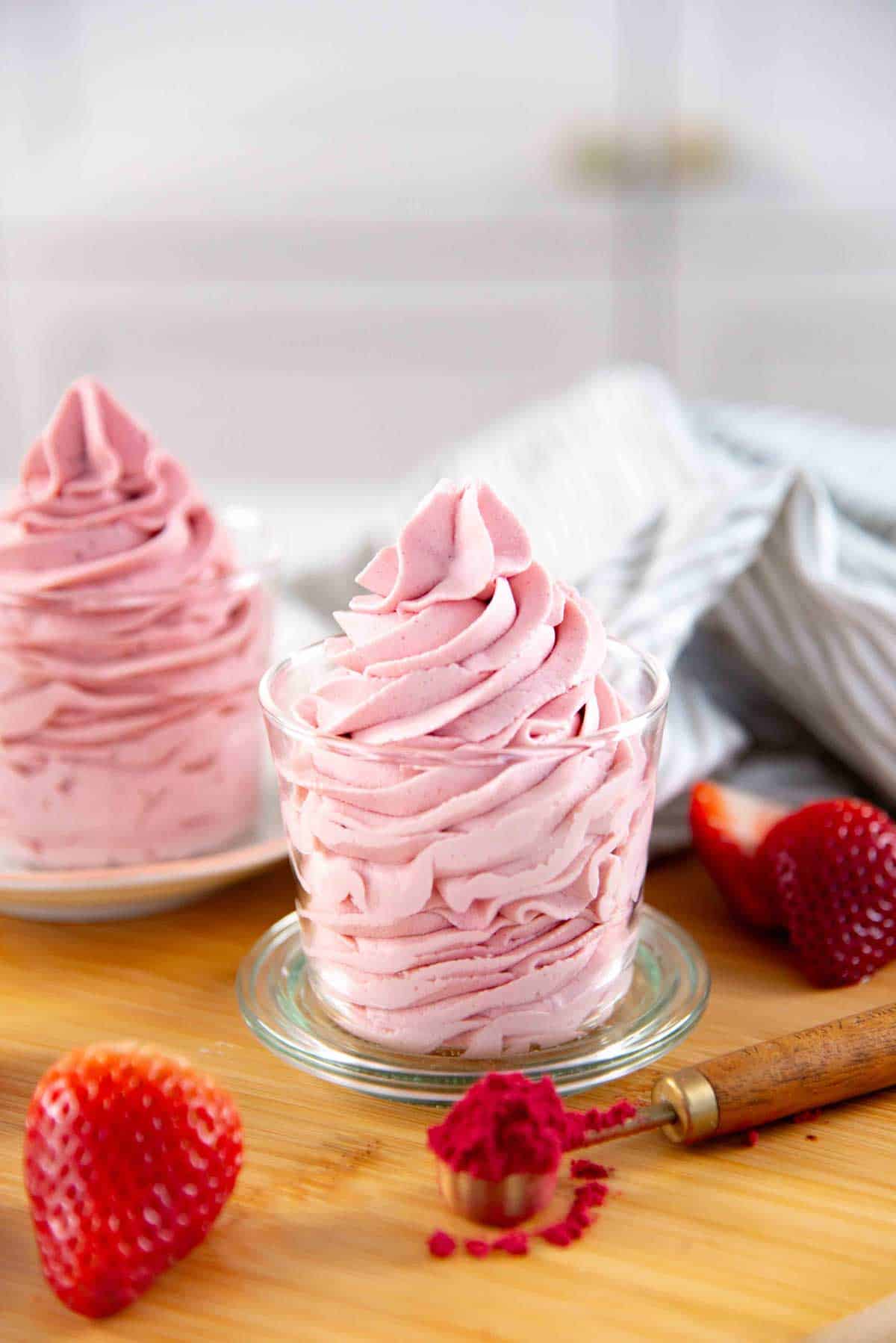 Close up of a big swirl of fluffy strawberry whipped cream in a small glass cup.