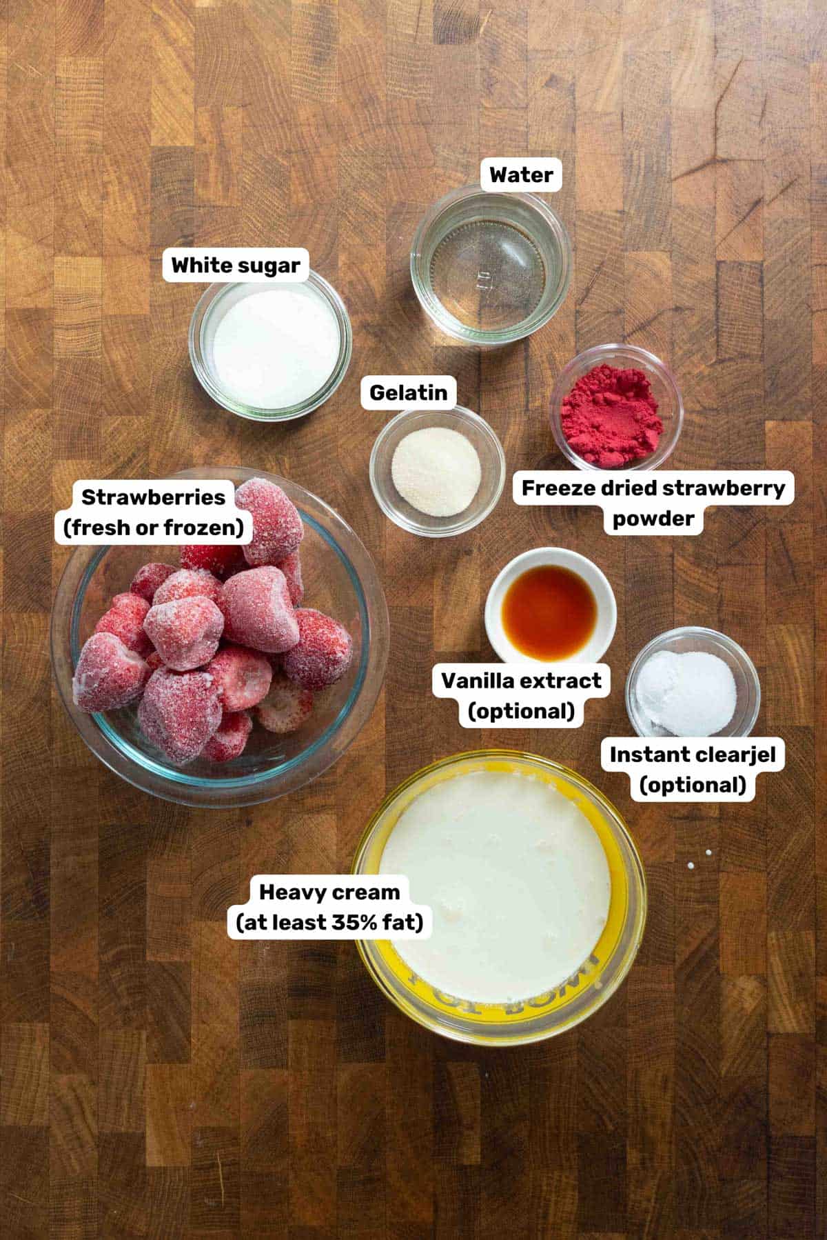 Labeled ingredients to make strawberry whipped cream in bowls on a wooden surface.