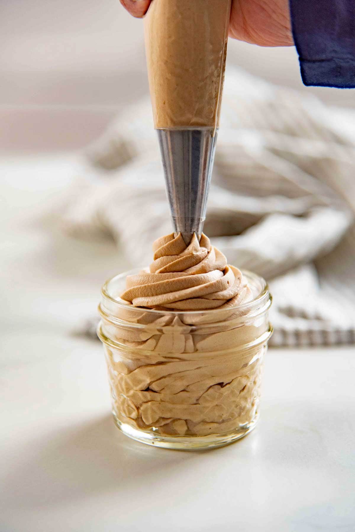Piping a swirl of coffee whipped cream into a small glass cup.