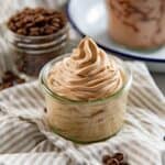 Close up of the fluffy coffee whipped cream piped into a small glass jar, with coffee beans in another jar behind it.