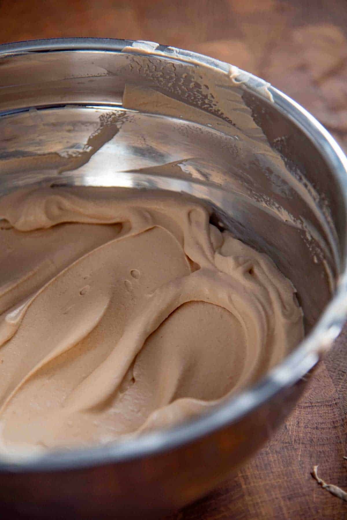 Close up image of creamy, fluffy, smooth coffee whipped cream in a metal mixing bowl.