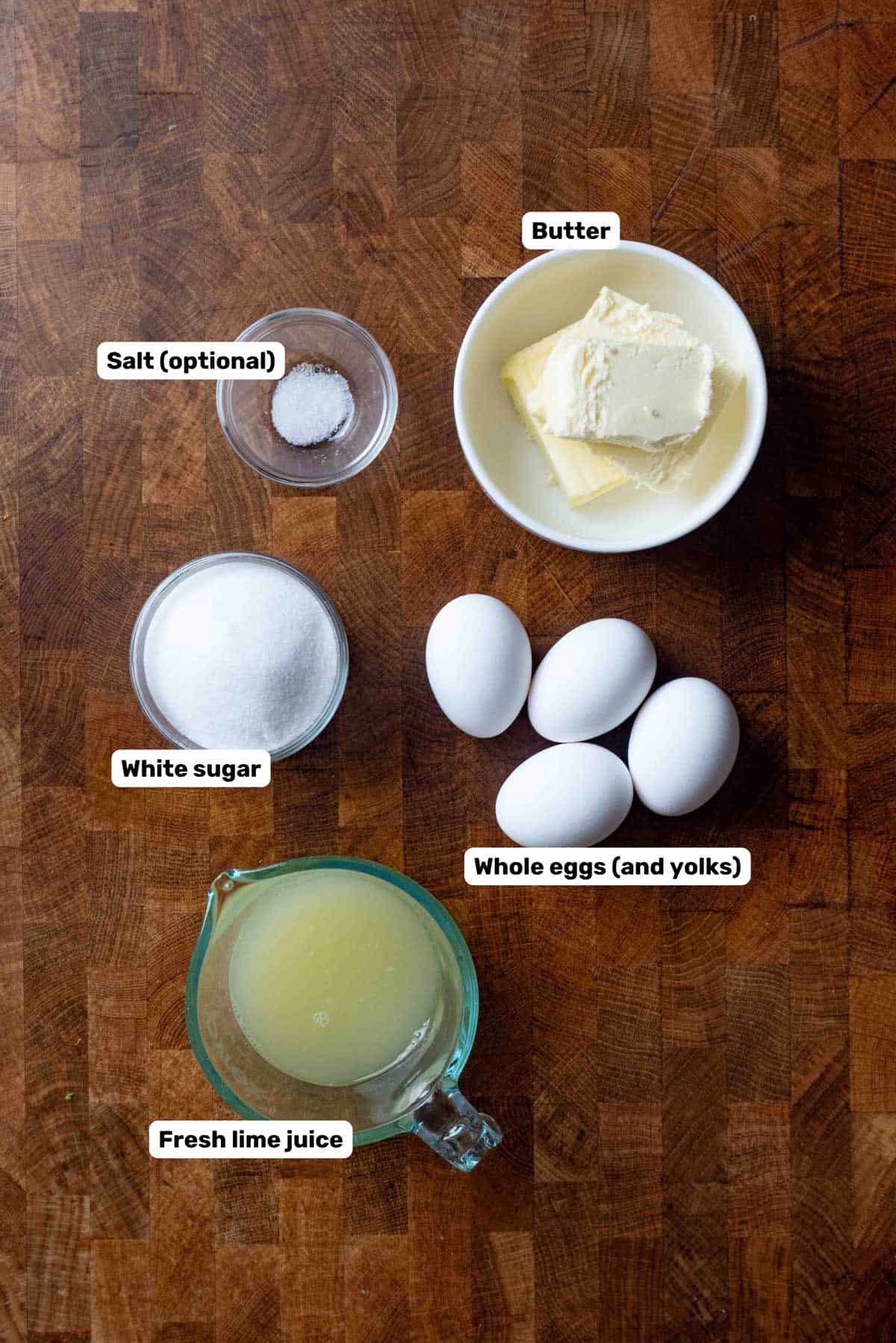 Labeled ingredients to make homemade lime curd sitting on a wooden counter.