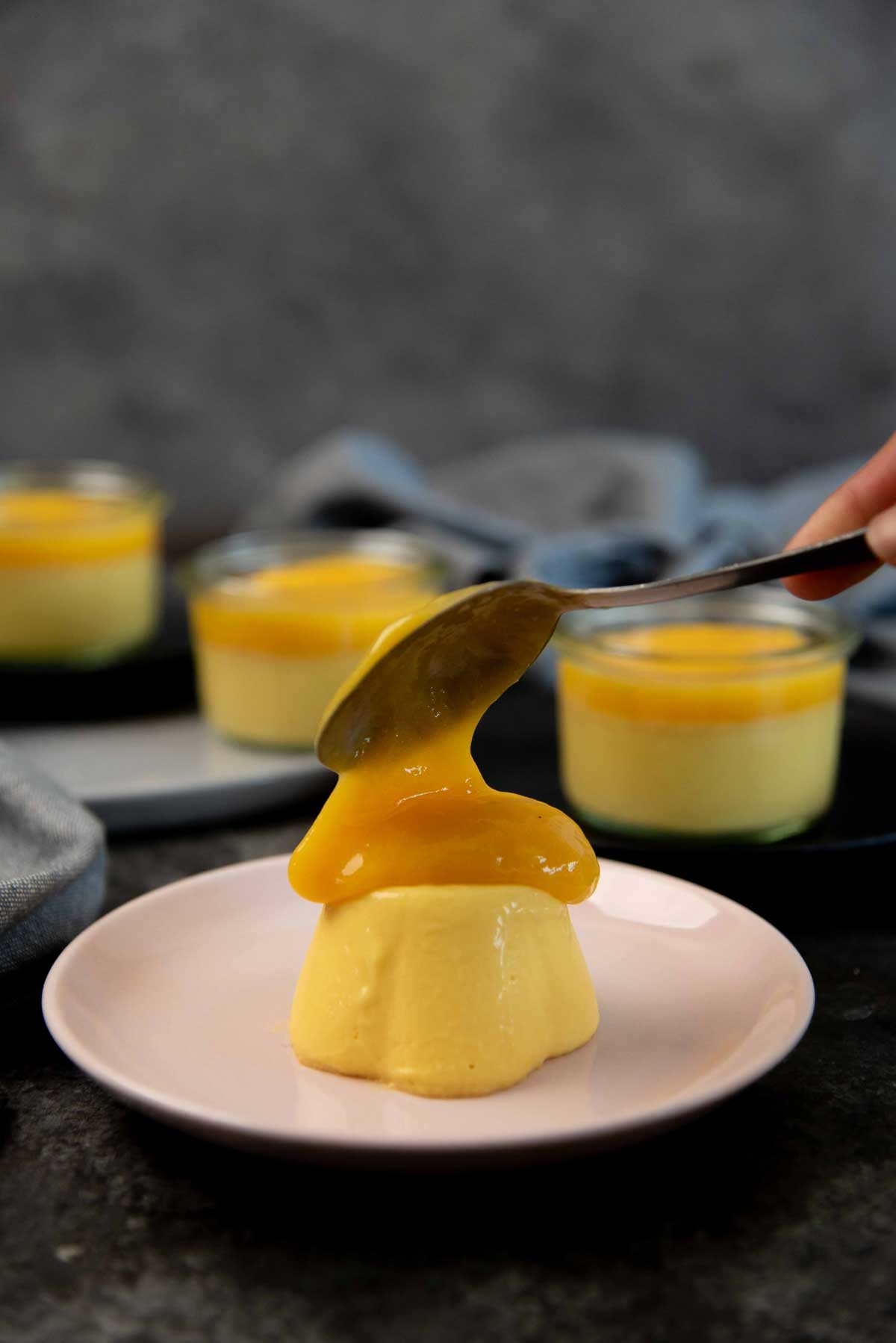 Dolloping mango gel over an unmolded mango panna cotta on a small pink serving plate.