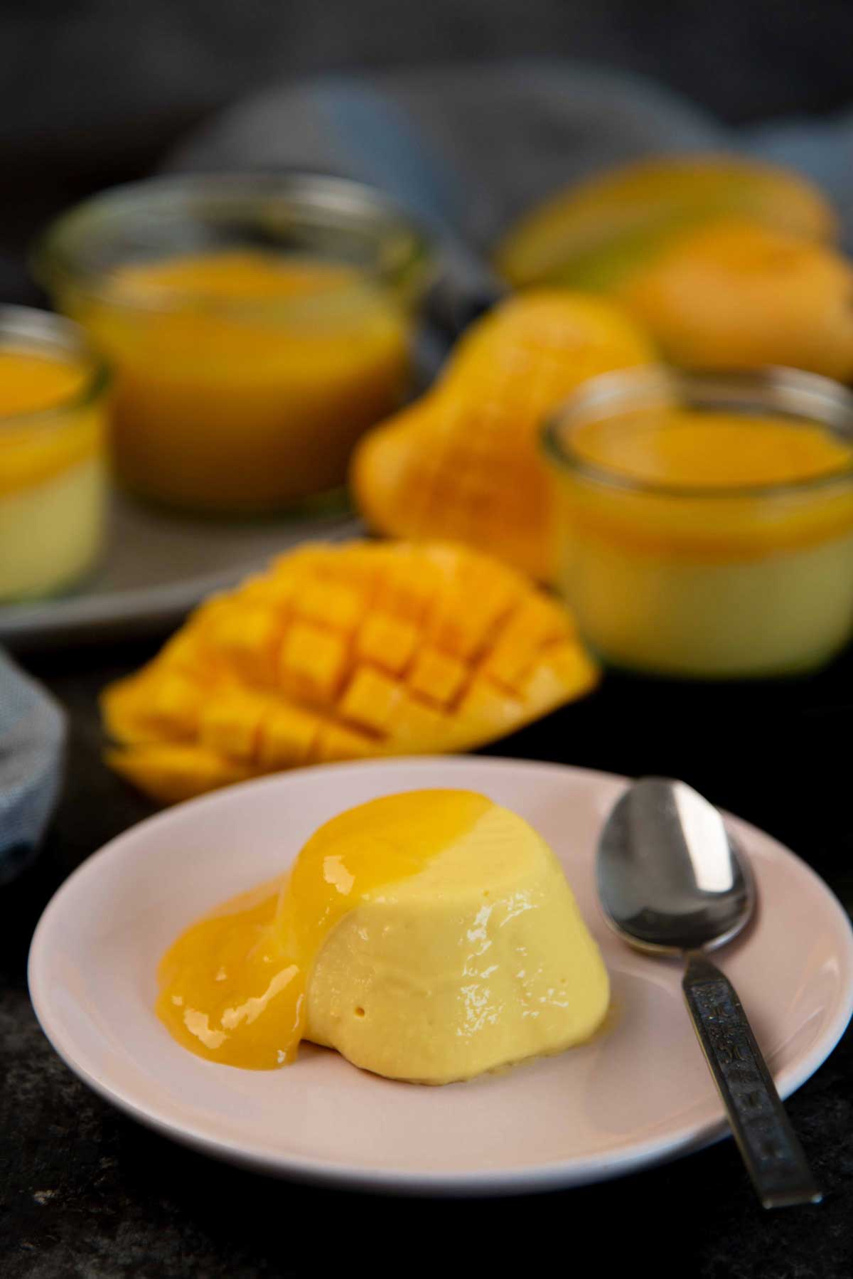 Unmolded mango panna cotta on a small pink serving plate topped with mango gel. A spoon is beside it.