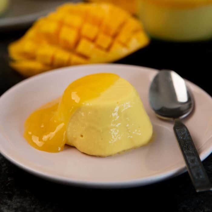 Unmolded mango panna cotta on a small pink serving plate topped with mango gel, with a spoon beside it.