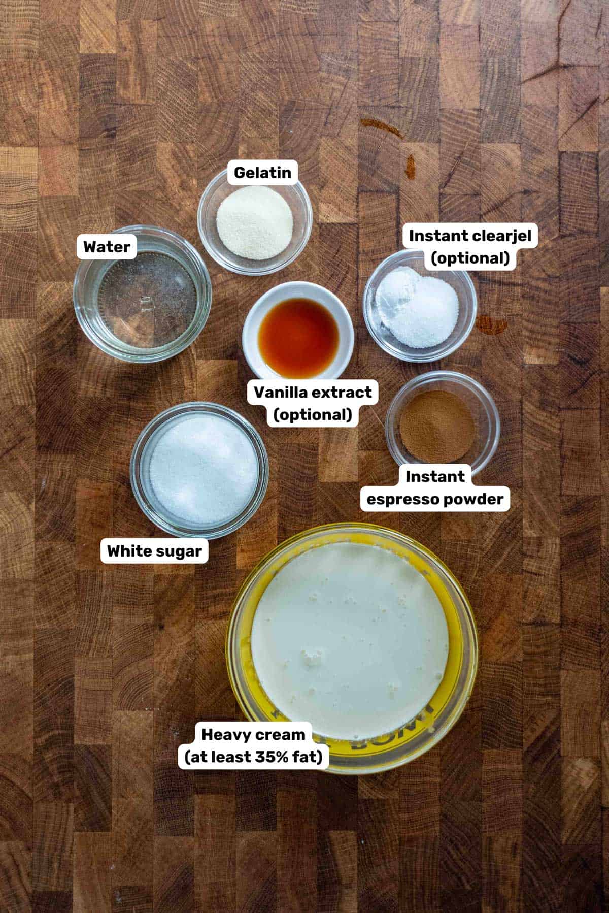 Labeled ingredients needed to make coffee whipped cream placed in small bowls on a wooden surface.