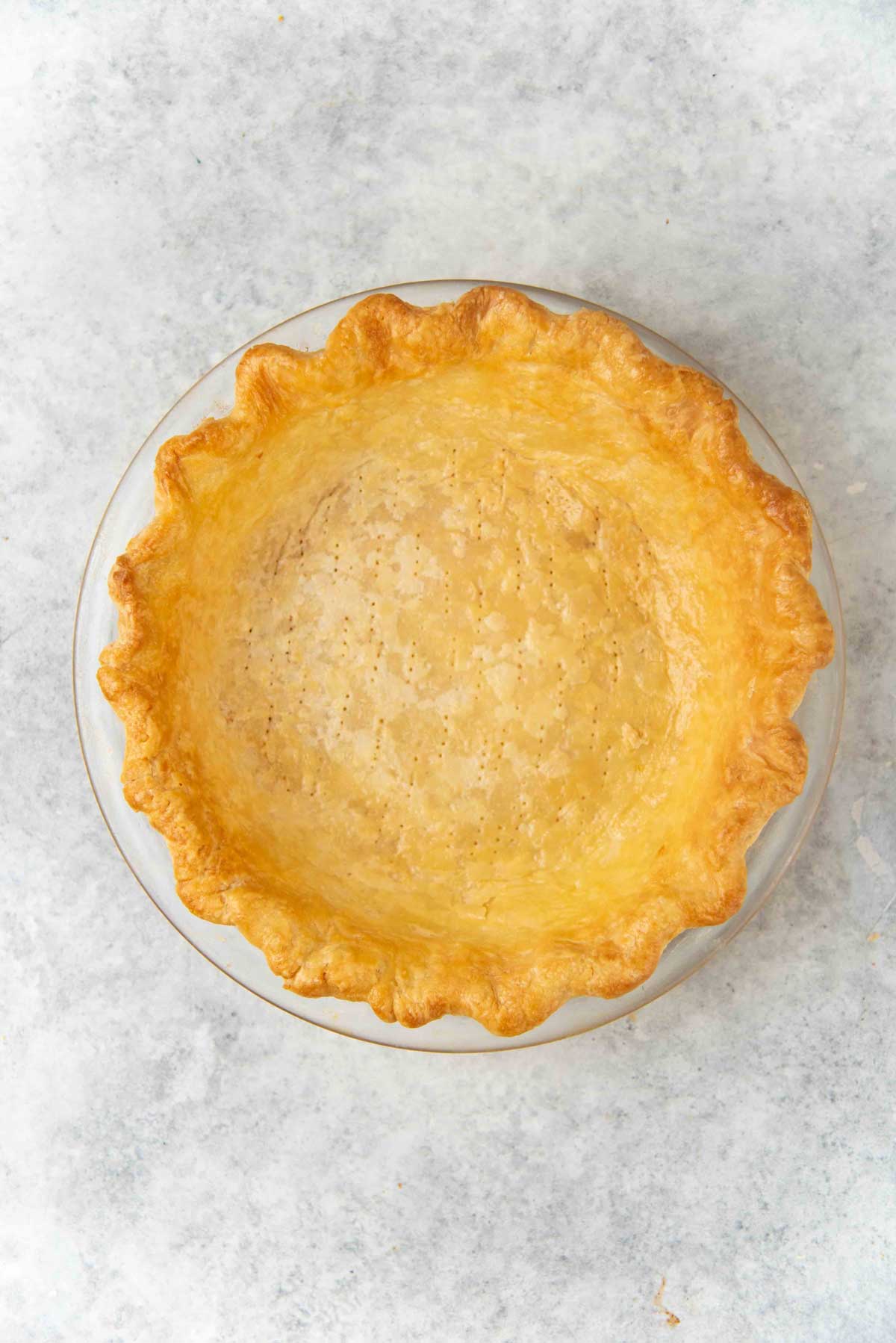 Golden brown fully blind baked pie crust in a round dish, with a crimped edge against a light background.