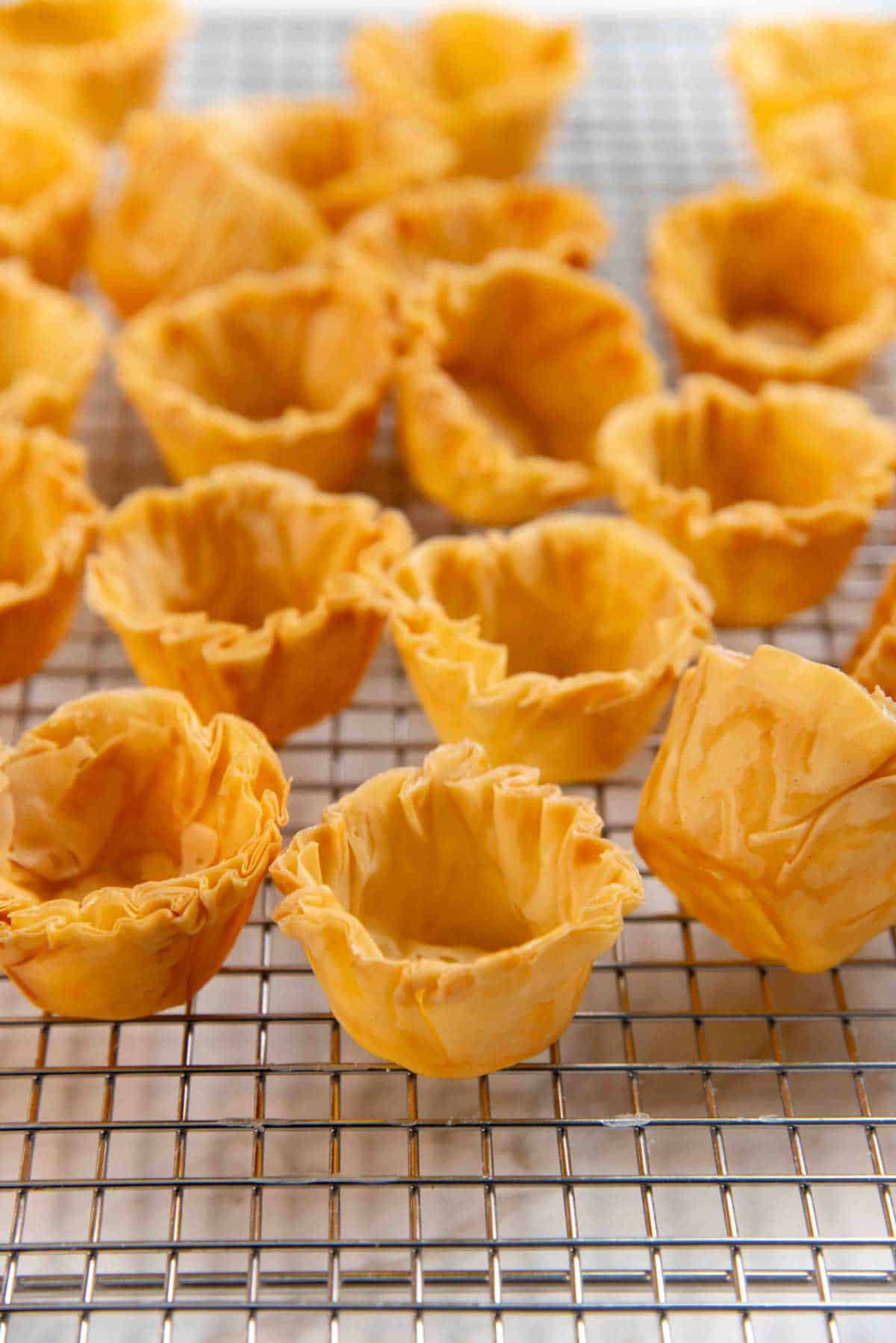 Close up of phyllo pastry shells with crisp, ruffled edges on a cooling rack.