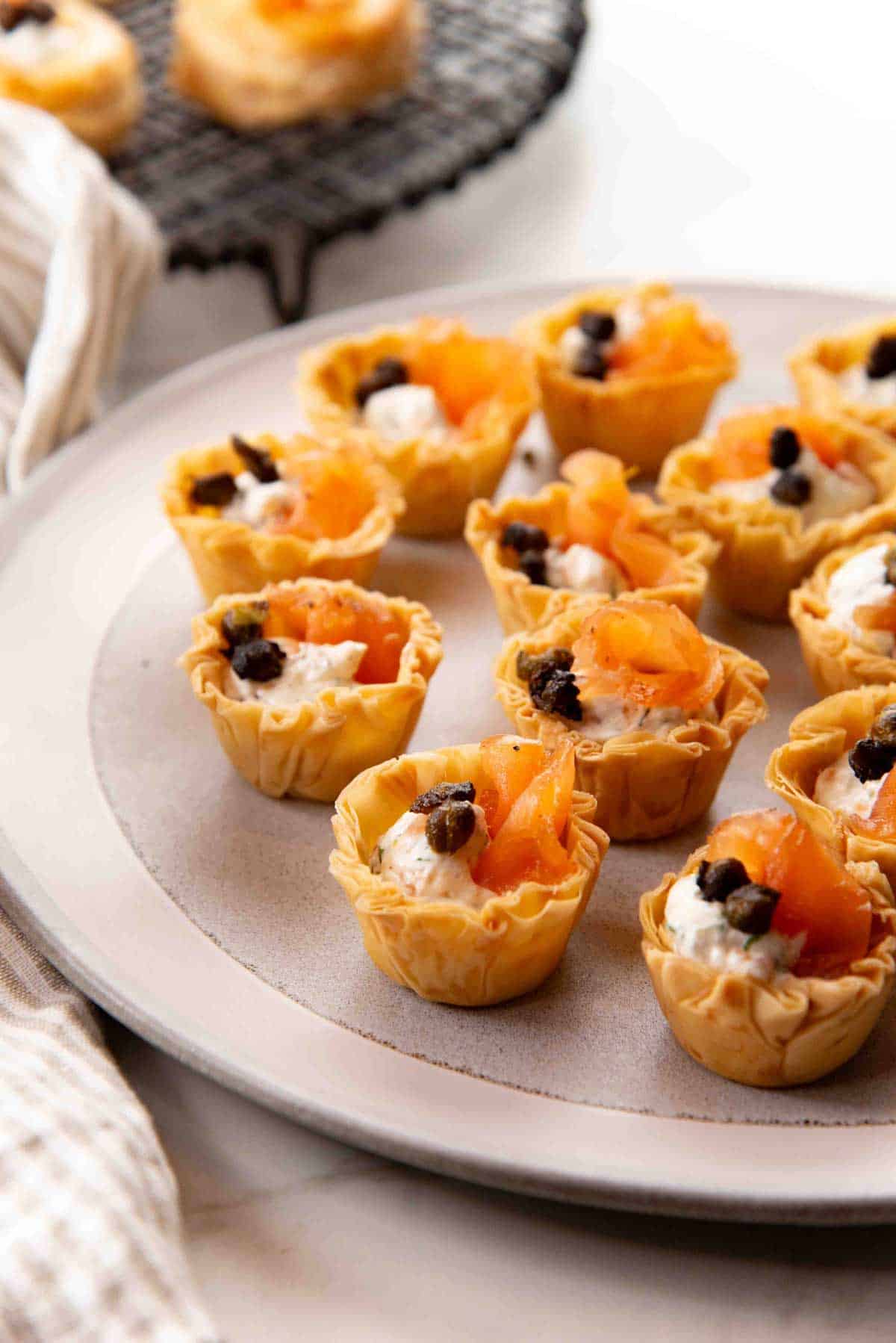 Phyllo cups filled with goat cheese and salmon arranged on a gray serving platter.