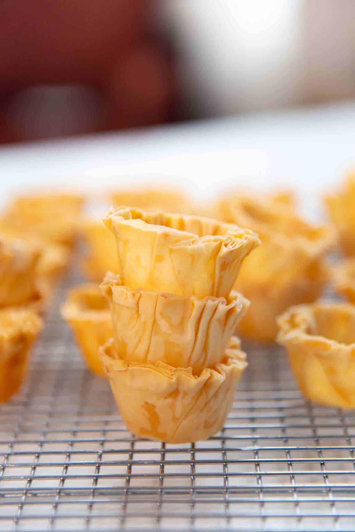 Baked, mini phyllo shells stacked on a cooling rack.