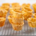 Close up of golden, flaky, crisp phyllo cups stacked on a cooling rack.