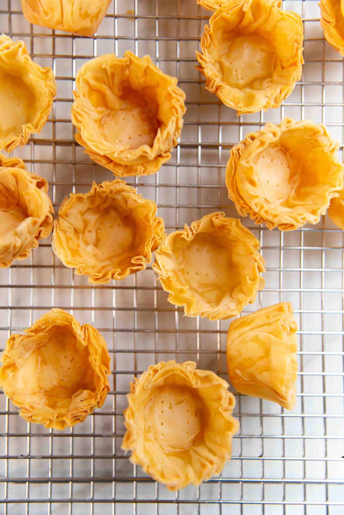 Overhead view of golden-brown phyllo cups with ruffled edges arranged on a cooling rack.