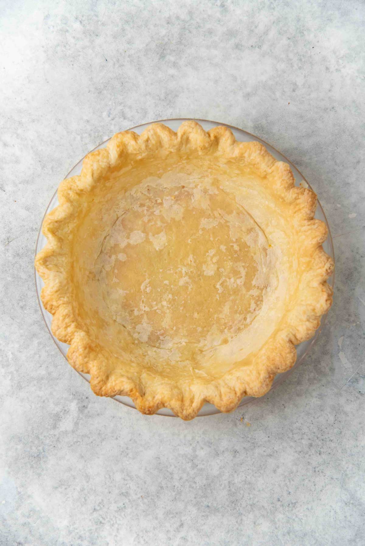 Par baked pie crust in a glass pie dish on a gray surface.