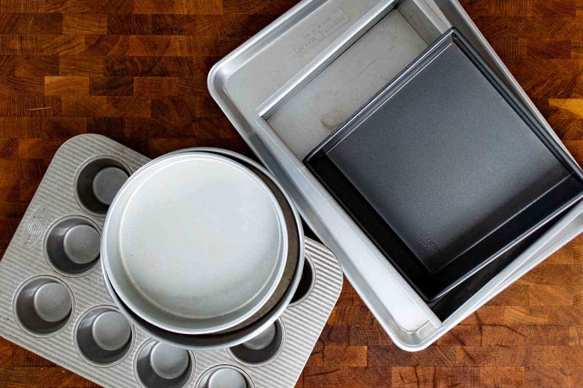 Baking pans on a wooden surface including half sheet pans, round cake pans, muffins pans, square and rectangle pans.