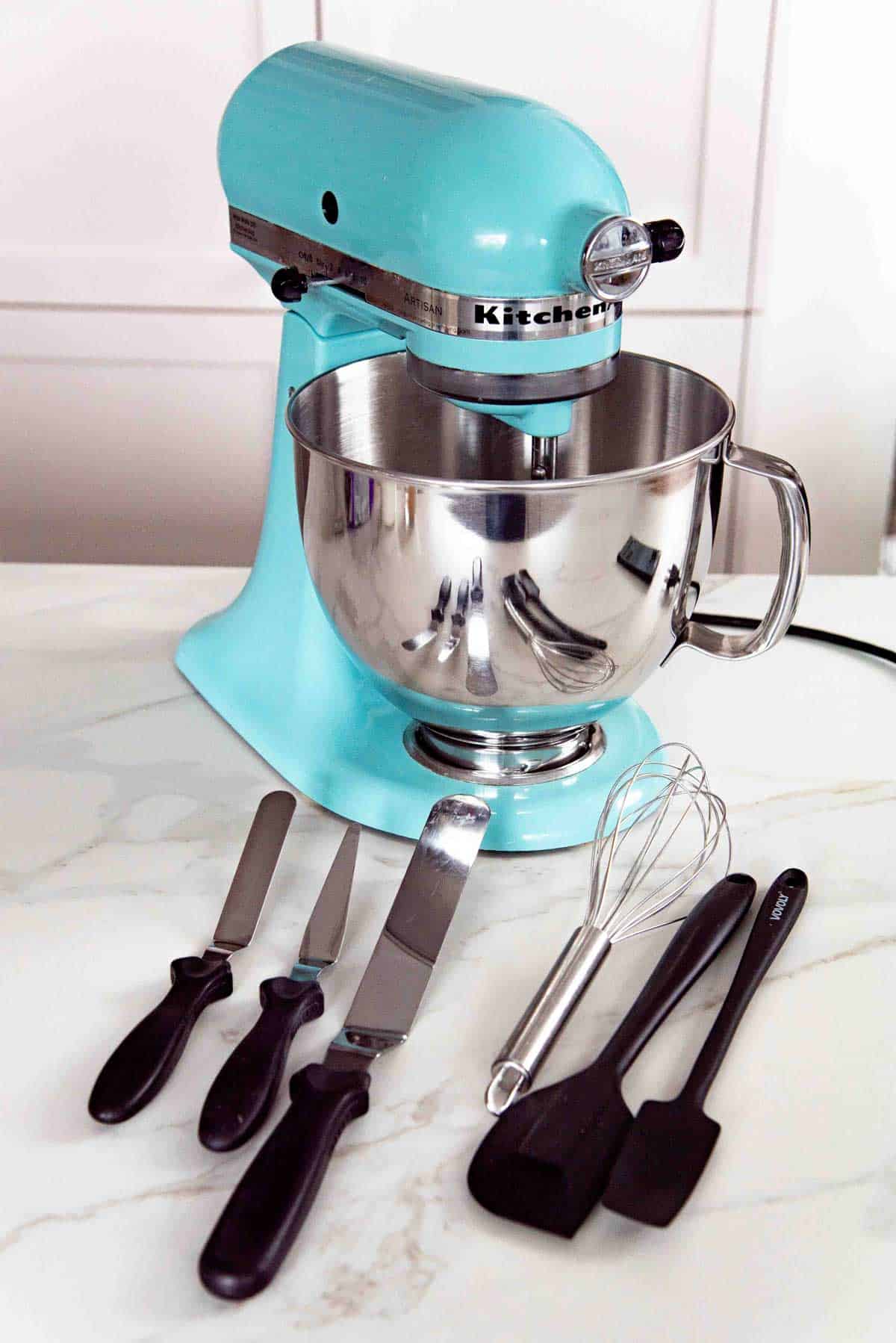 Stand mixer and baking tools to mix ingredients on a light countertop. Various rubber spatulas and whisks are also present.