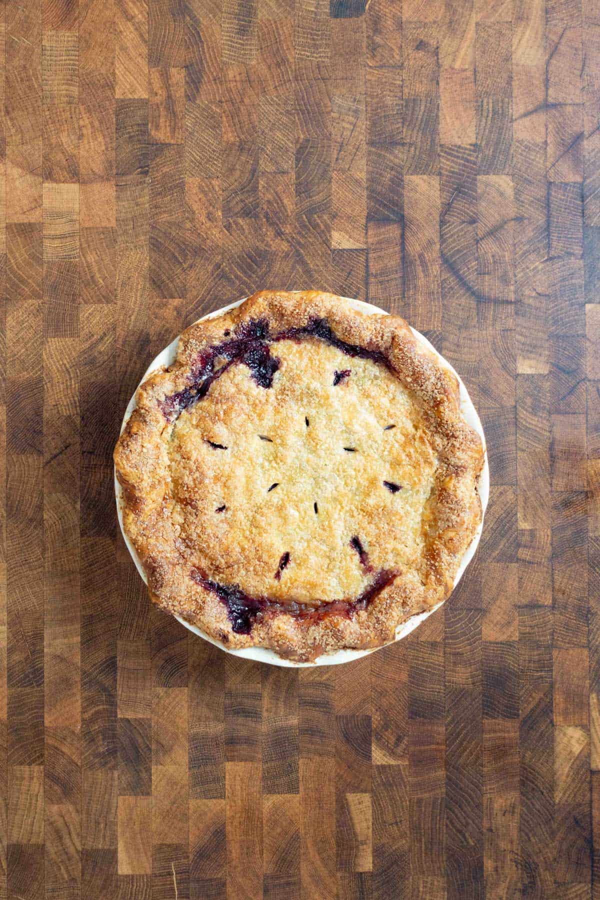 Freshly baked double crust round pie with a golden, flaky solid top crust on a wooden surface.
