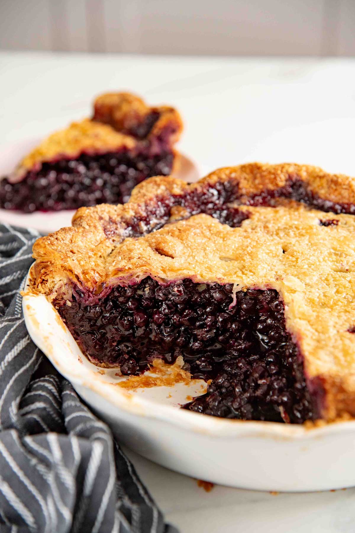 Golden-brown blueberry pie with a solid top crust, a slice removed, revealing juicy filling packed with small wild blueberries.