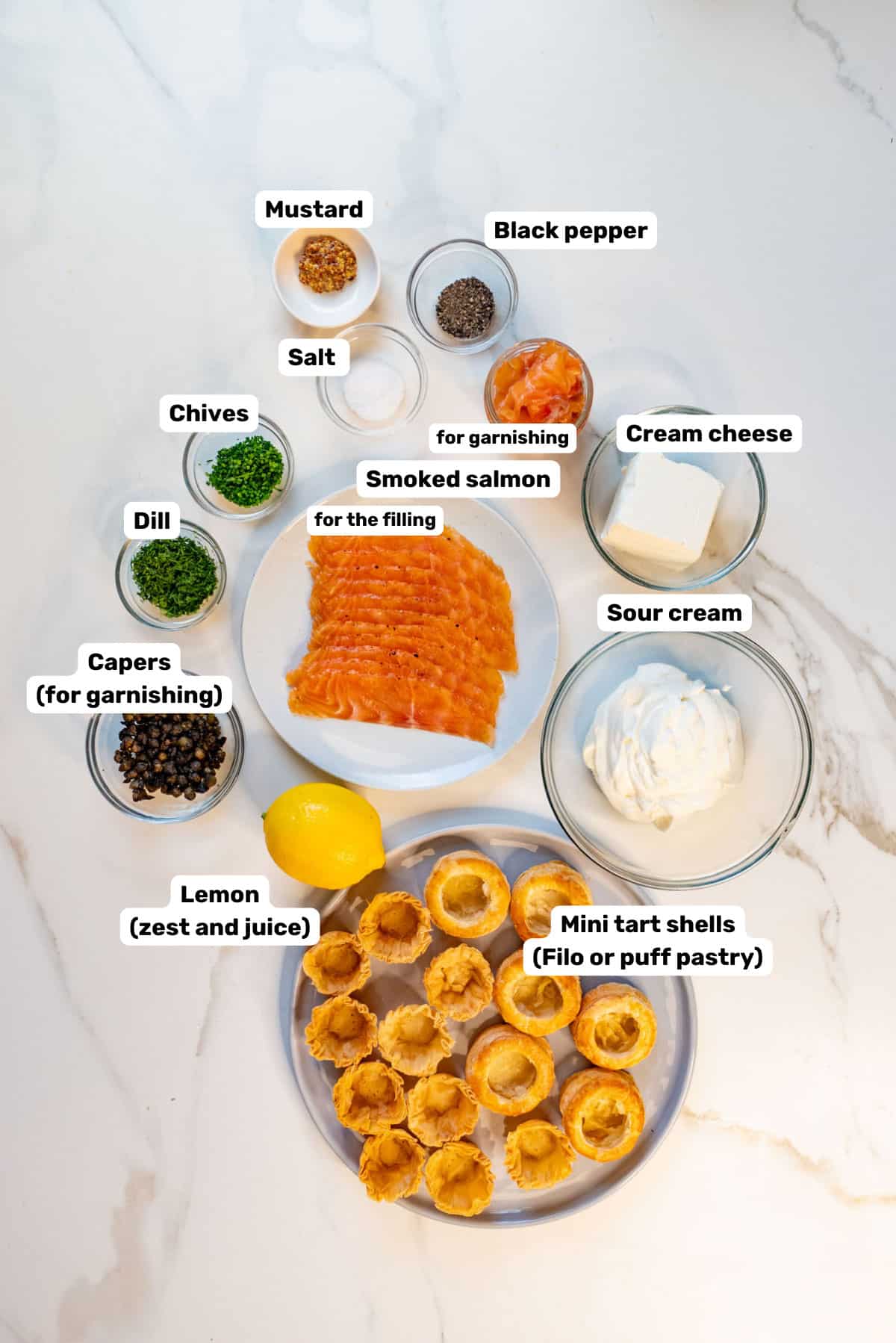 Labeled ingredients to make smoked salmon canapes on a white counter.
