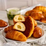 Several salt bread rolls on a plate showing the crisp bottom on one, salt flakes on top, and the butter hole in a bread roll that's cut in half.
