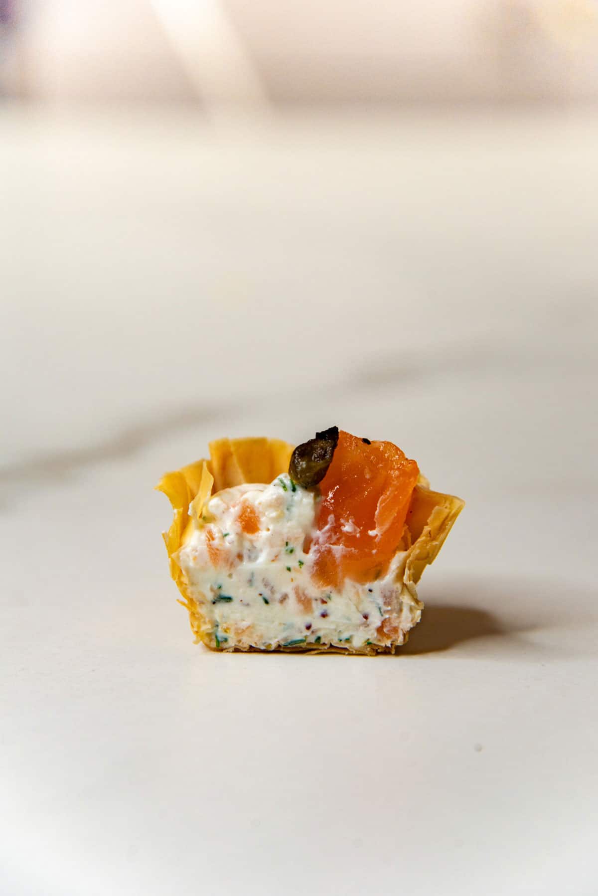 Cross section of a smoked salmon canape in a phyllo cup showing the cream cheese filling with chopped herbs and lemon zest.