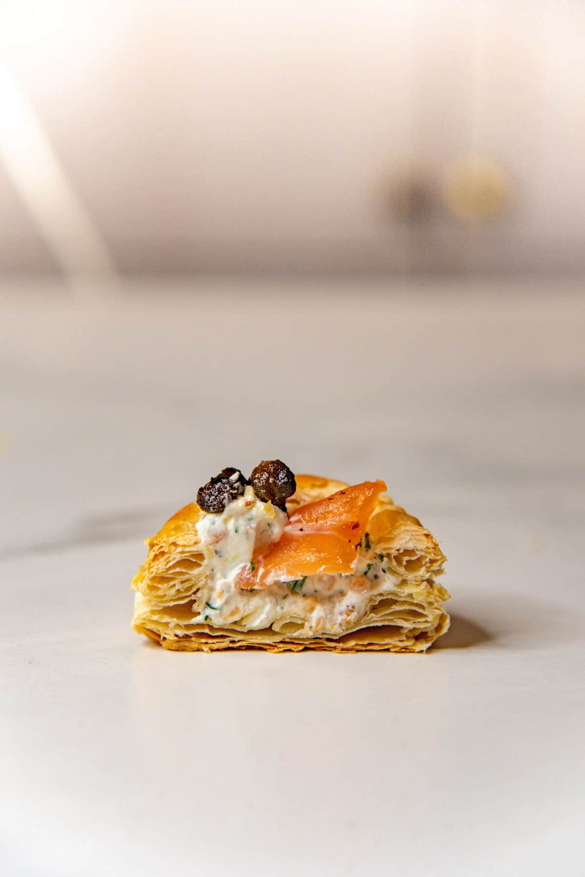 Cross section of a smoked salmon canape in a mini puff pastry tart showing the cream cheese filling with chopped herbs and lemon zest.