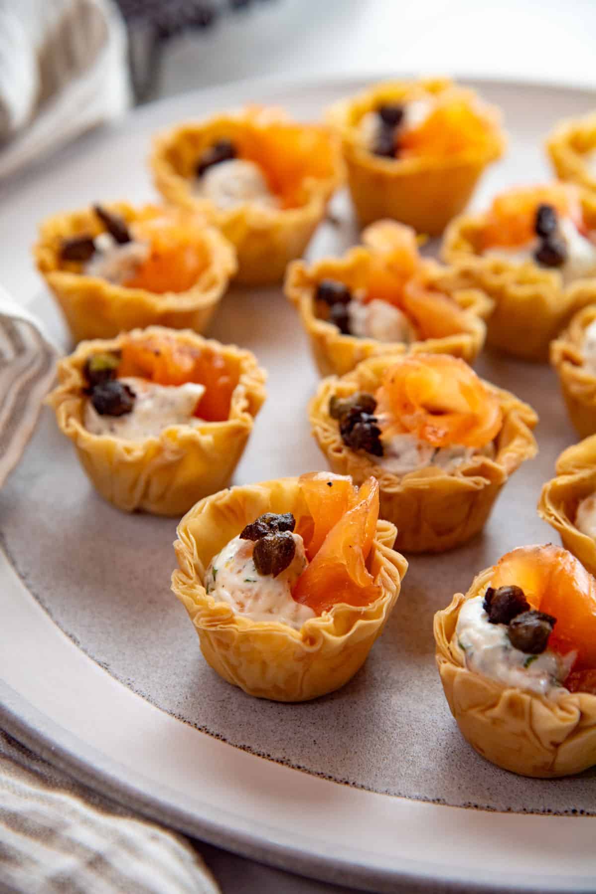 Smoked salmon appetizers with cream cheese filling and capers served in phyllo pastry cups on a plate.