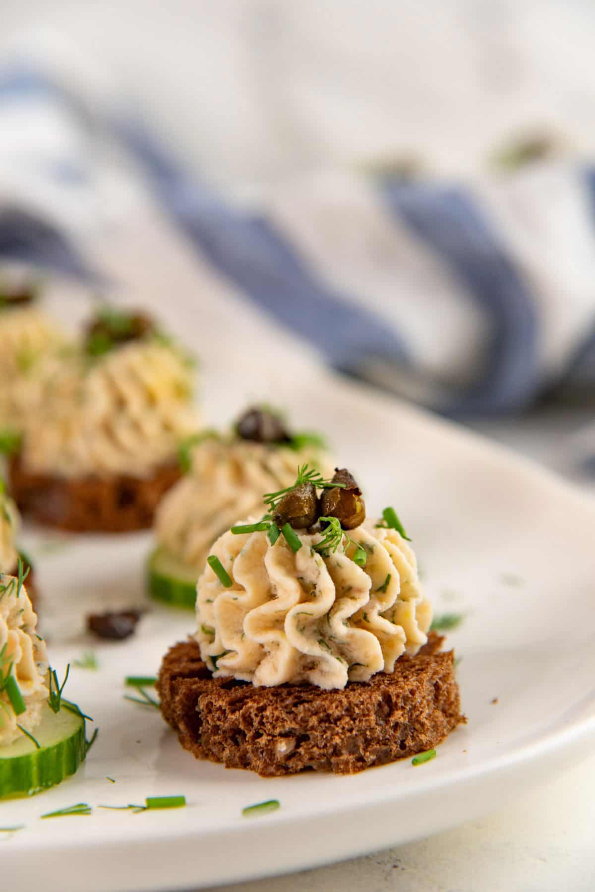 Close up of salmon mousse piped onto a rye bread slice and topped with capers and chopped herbs.