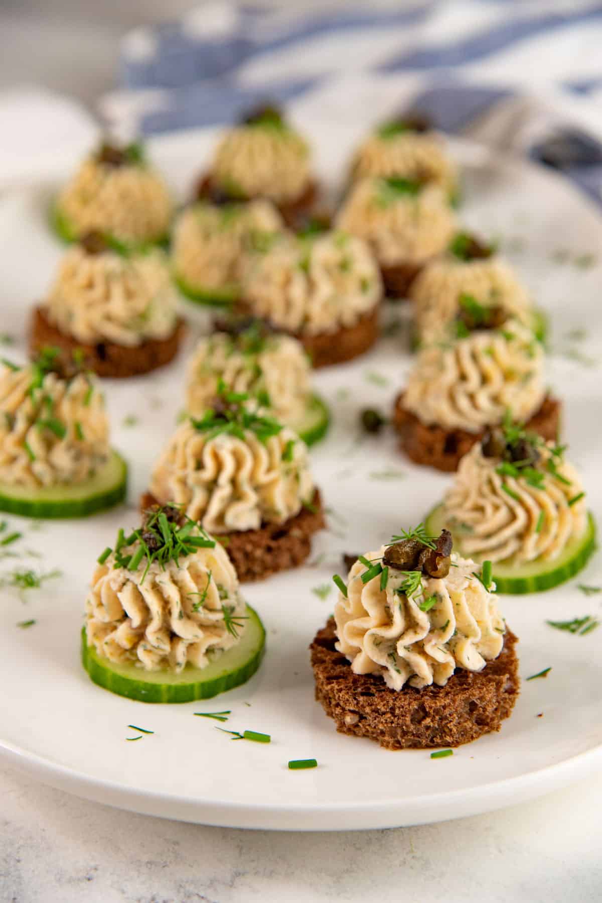 A serving platter of salmon appetizers featuring salmon mousse on top of cucumber and rye bread slices.