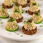 Smoked salmon mousse served with cucumber and rye bread slices and topped with chopped herbs and capers.