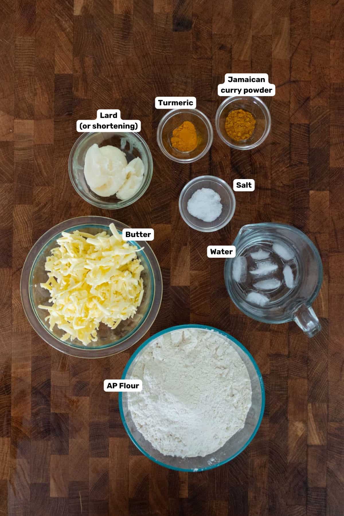 Labeled ingredients to make the Jamaican beef patty dough on a wooden surface.