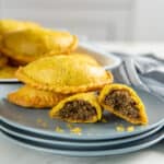 A Jamaican beef patty broken in half to show the juicy beef filling in the middle. Two whole patties are in the background.