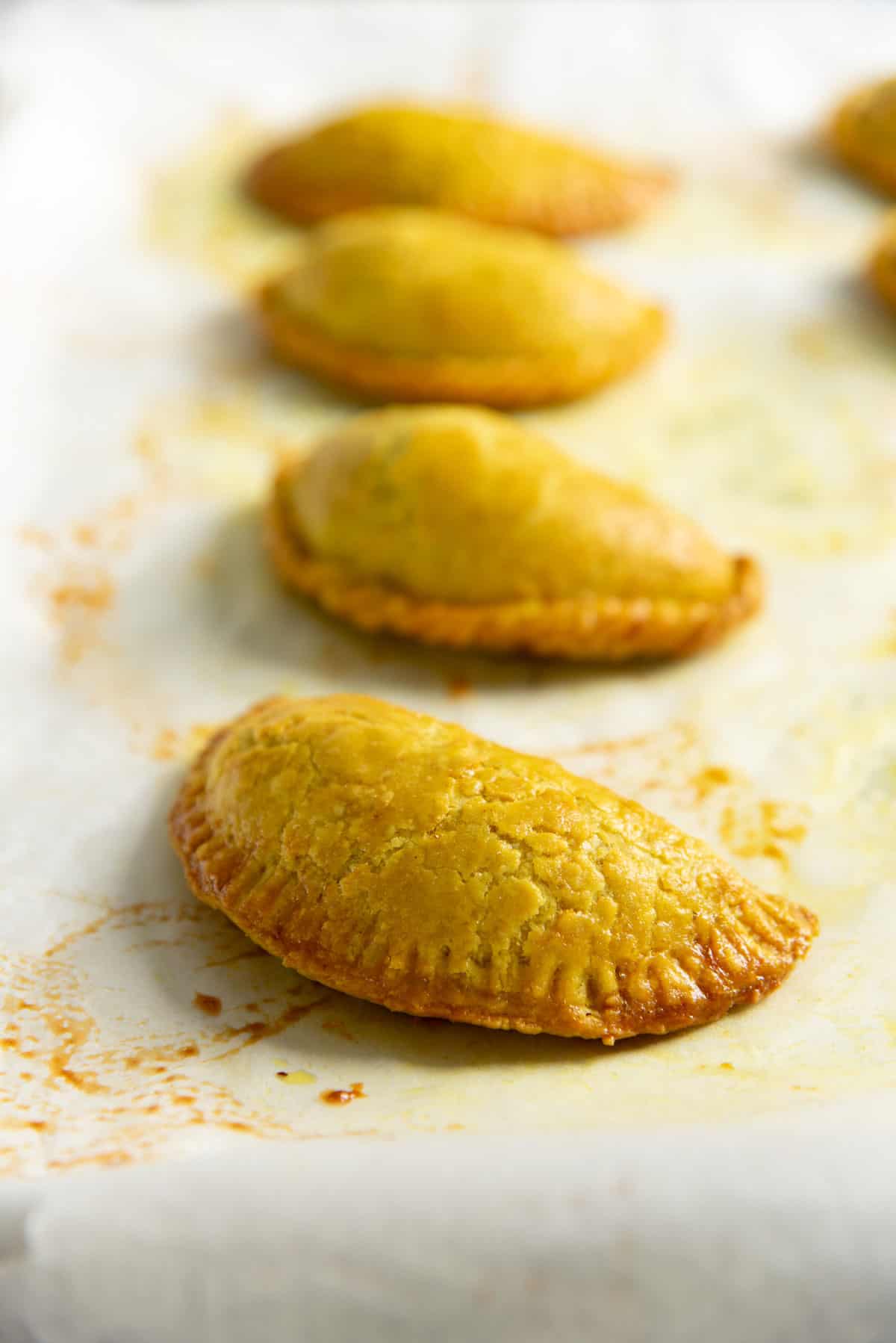 Four freshly baked, yellow Jamaican beef patties placed on parchment paper.