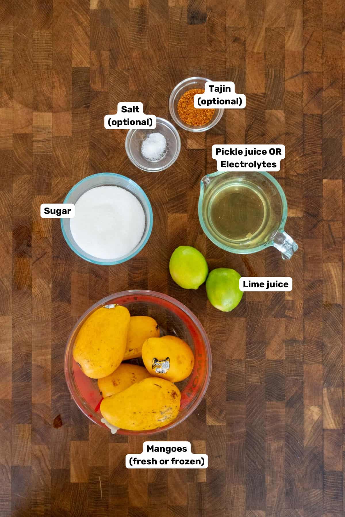 Labeled ingredients to make mango popsicles on a wooden surface.