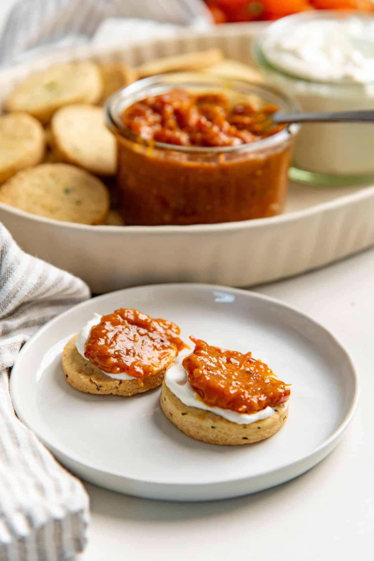 Two cheese cookies on a white plate topped with a white spread and chunky tomato bacon jam.