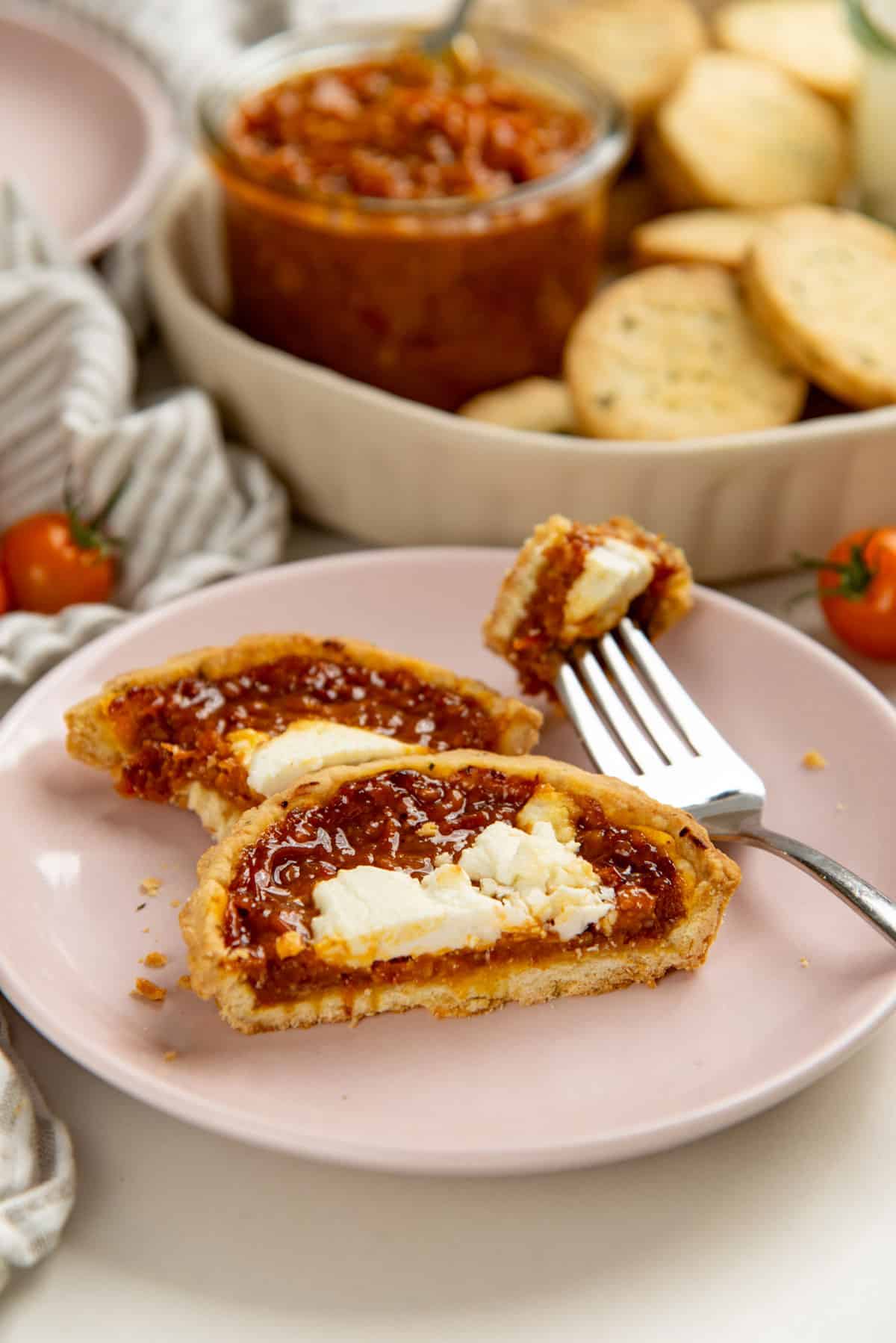 Savory tomato tart filled with bacon tomato jam cut in half and served on a small pink plate.