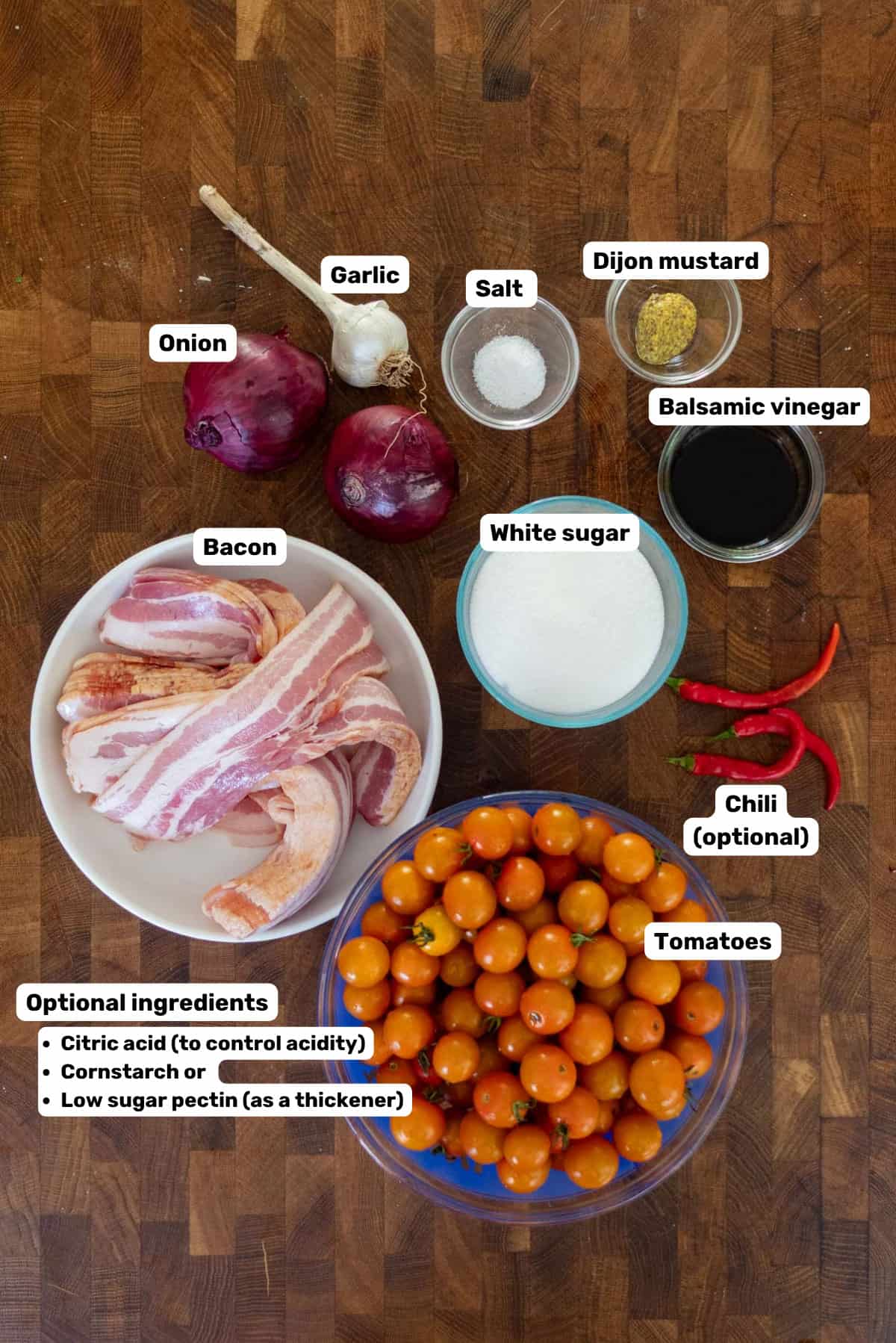 Labeled ingredients to make bacon tomato jam on a wooden surface.
