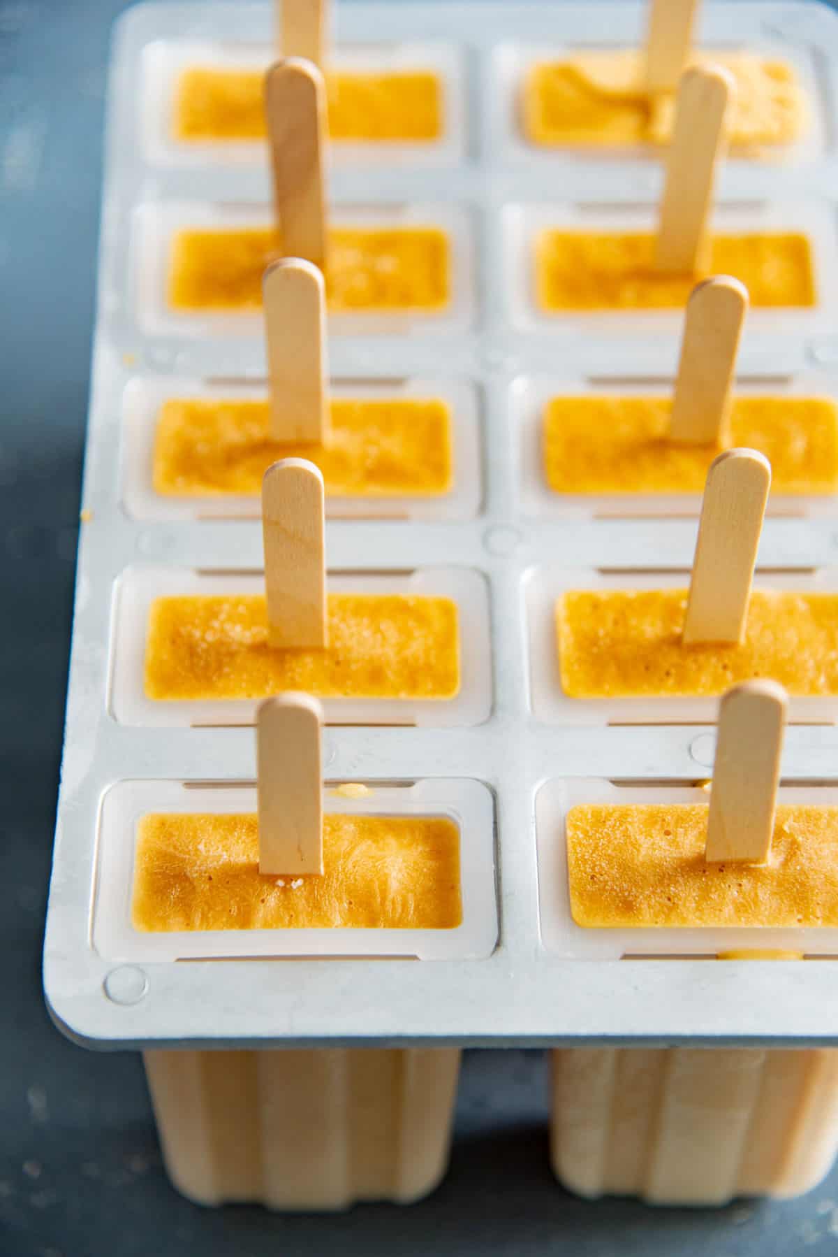 A set of ten popsicle molds with frozen peach popsicles, with the popsicle sticks sticking out of them.