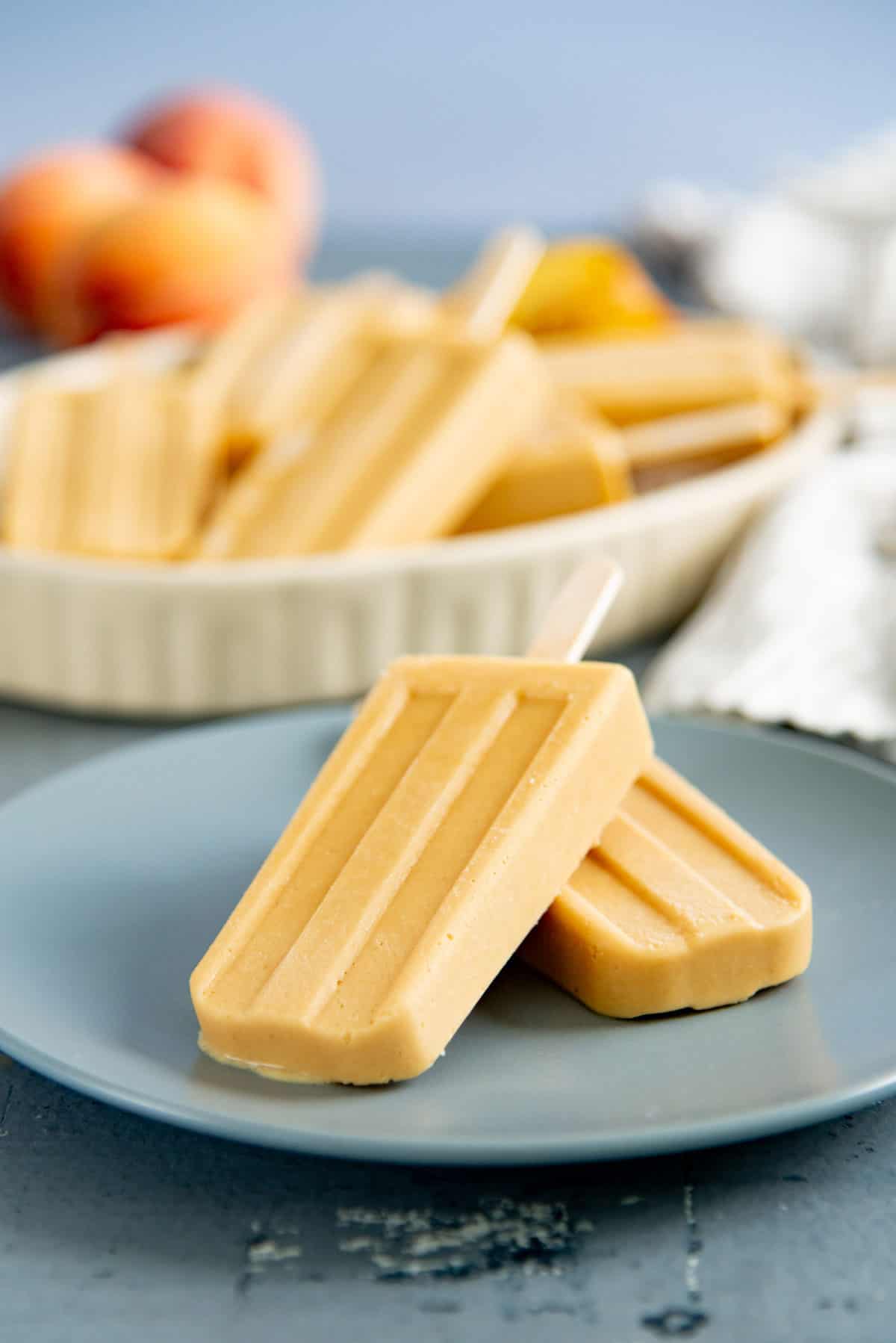 Close up of two popsicles placed on a small blue plate. More popsicles in a dish in the background.