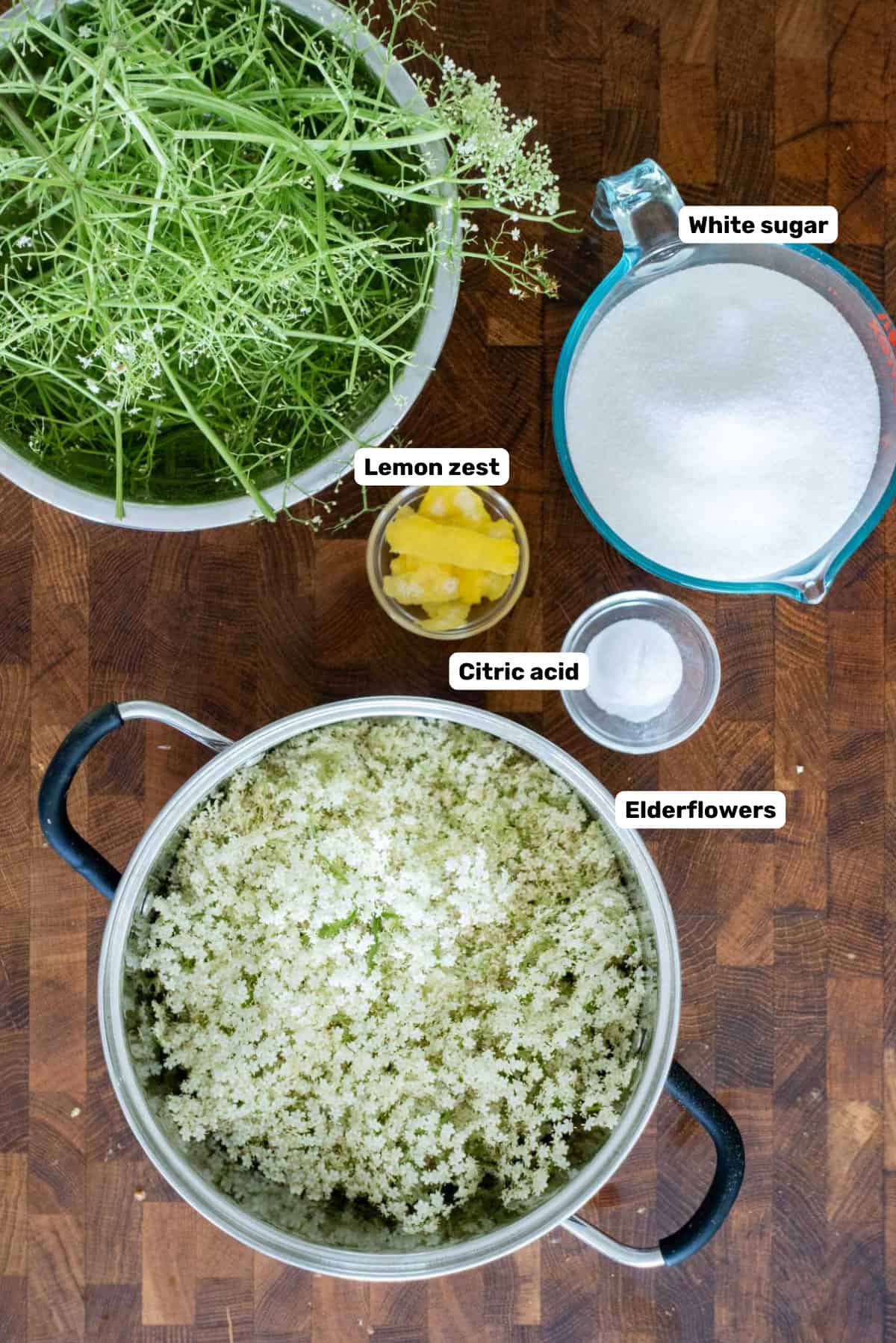 Labeled ingredients needed to make elderflower cordial or syrup on a wooden surface.
