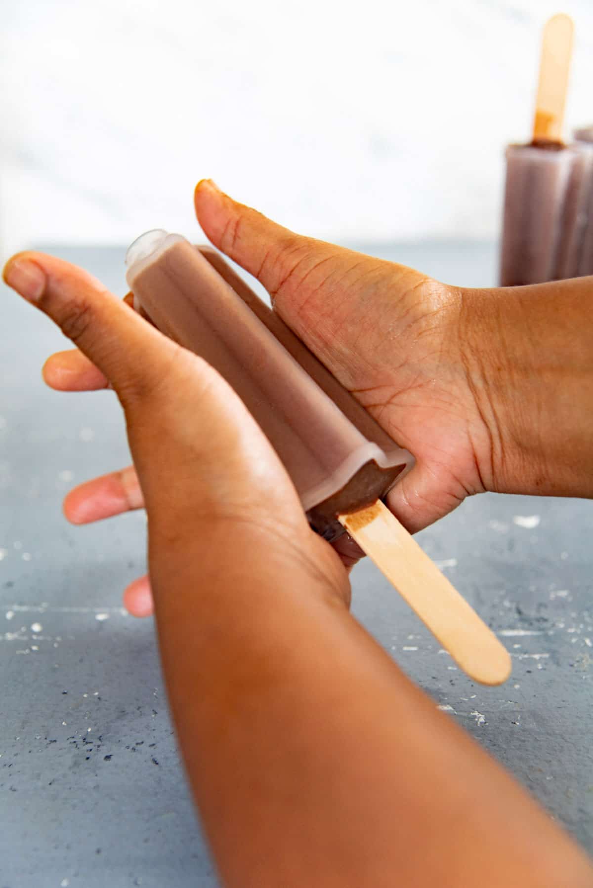 Two hands squeezing a frozen fudgesicle in a popsicle mold to help release it.
