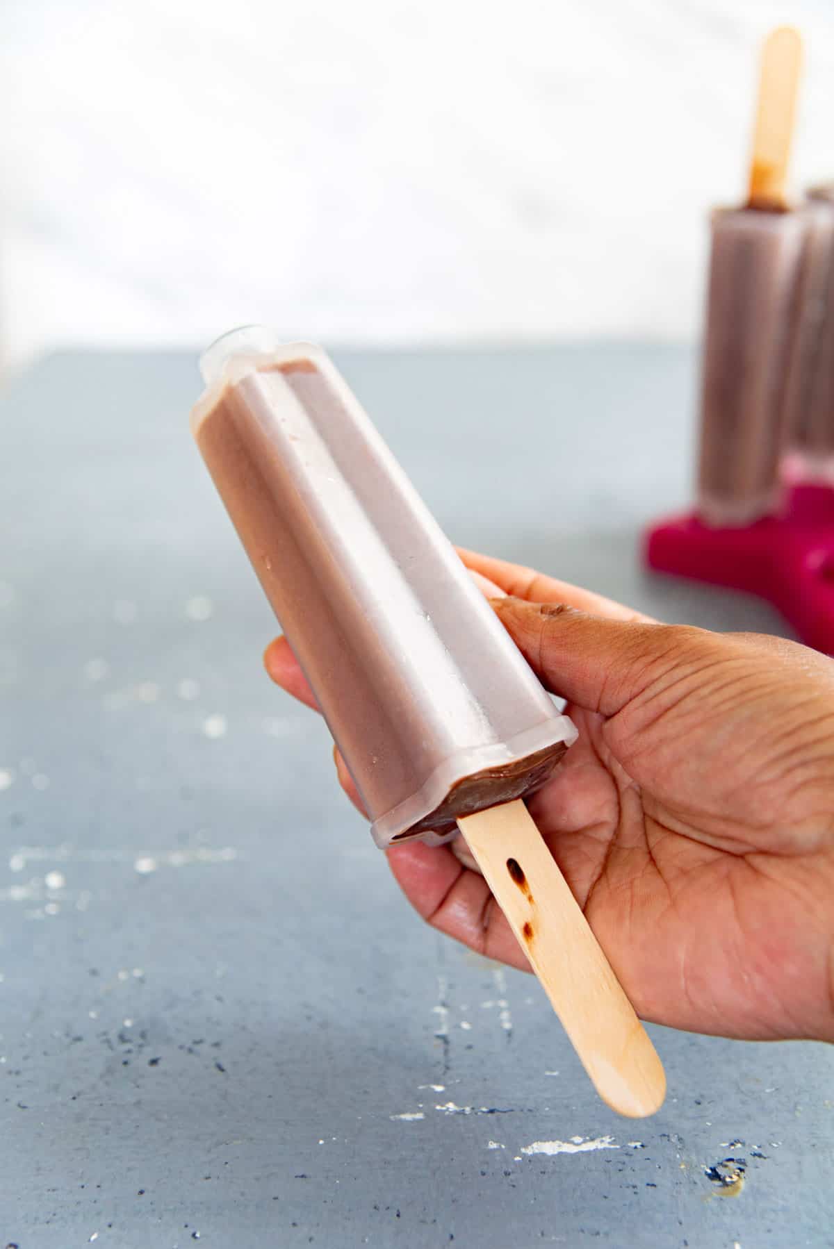 A hand holding up a chocolate fudgesicle in a plastic star popsicle mold.