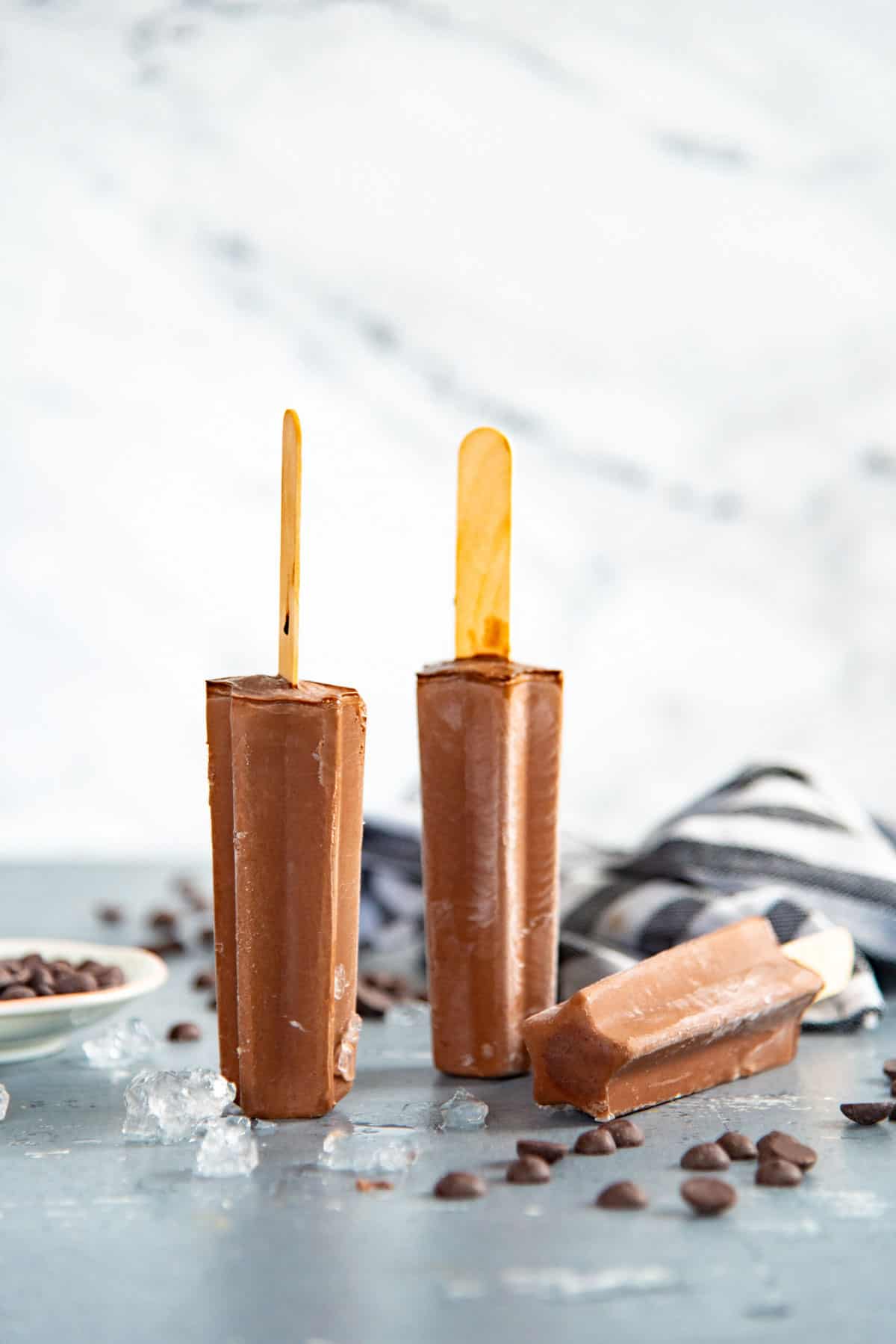 Two creamy fudgesicles standing on their head on a blue table. Another fudgesicle is laying on its side next to them.