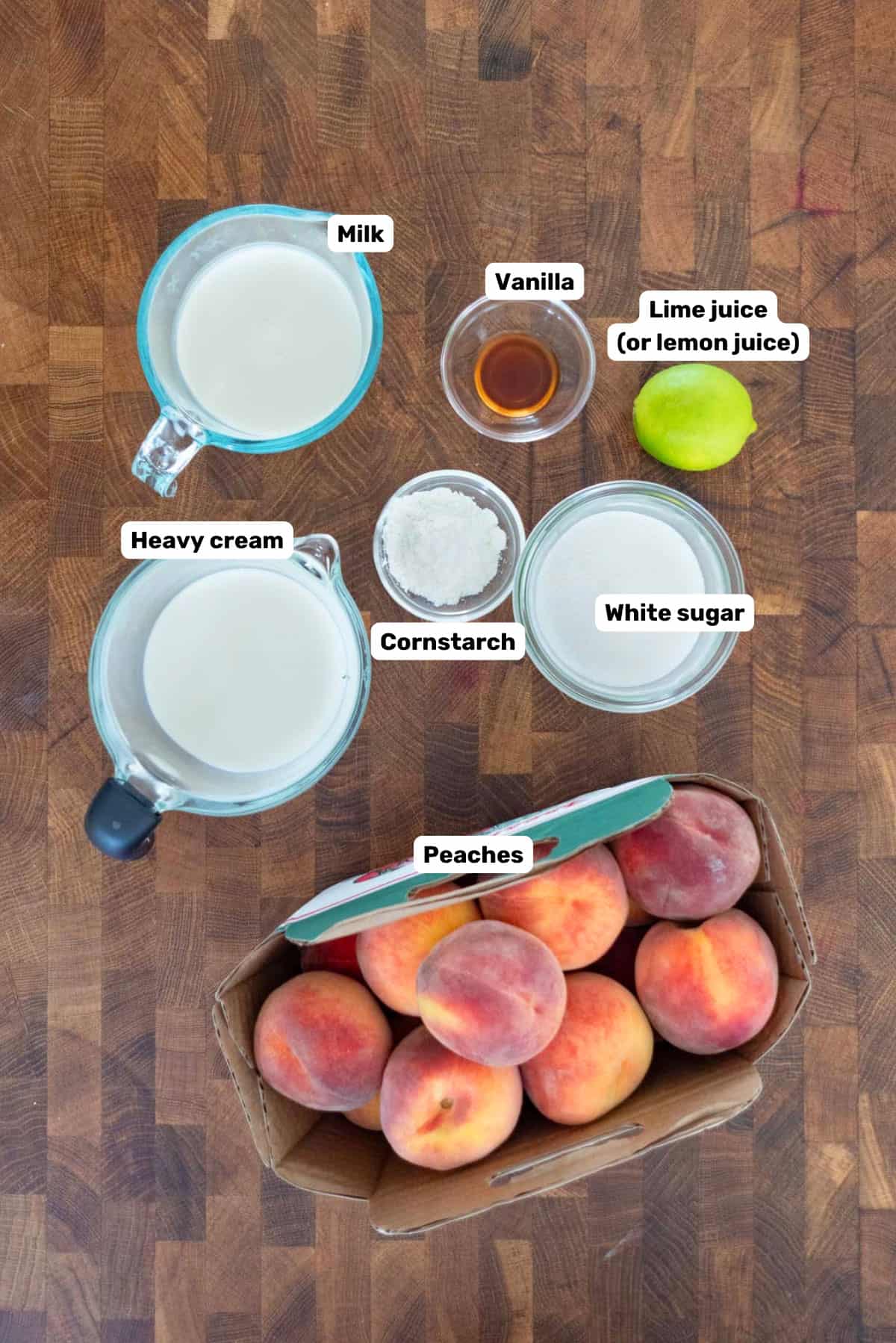 Labeled ingredients to make creamy peach popsicles on a wooden surface.