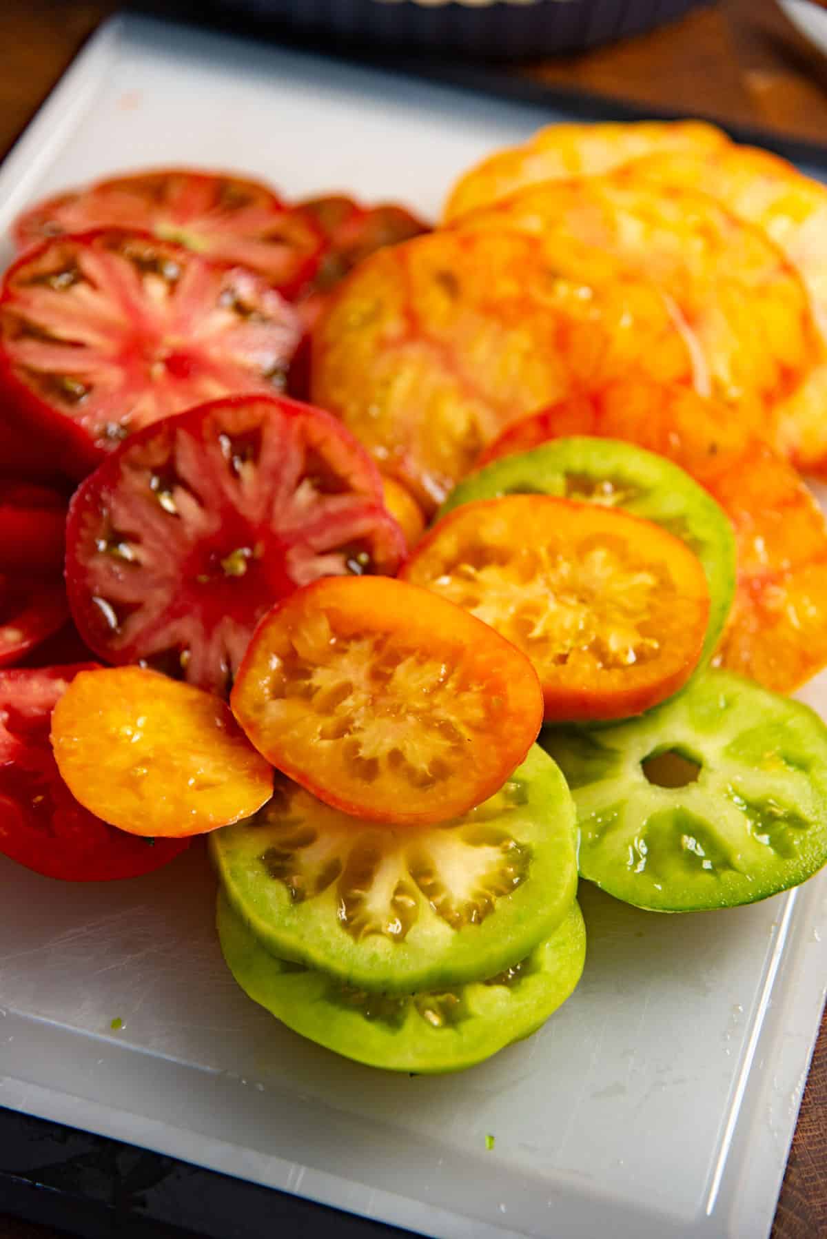 Close up of the green, yellow, red, and orange colored tomato slices on a cutting board.
