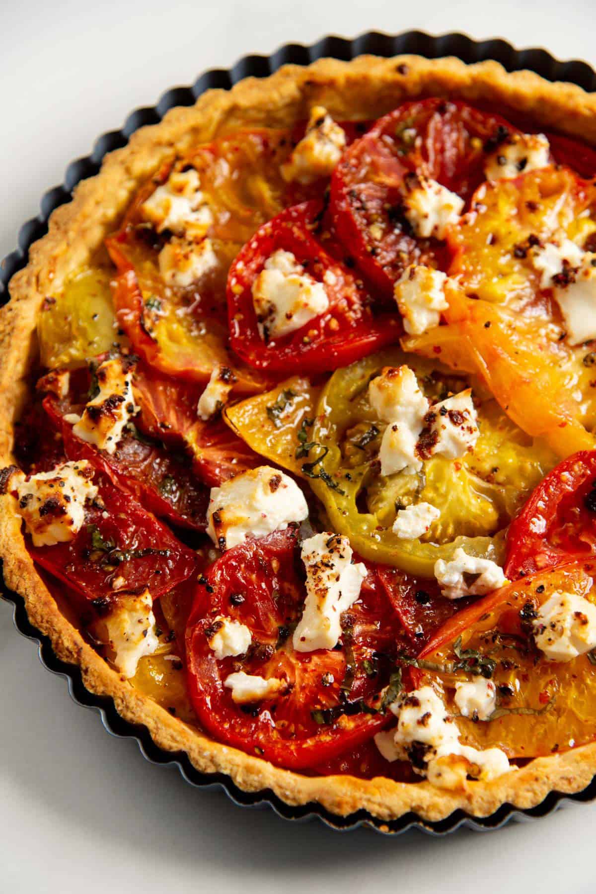 Close up of a freshly baked tomato tart with a golden crust and caramelized tomato slices and cheese.