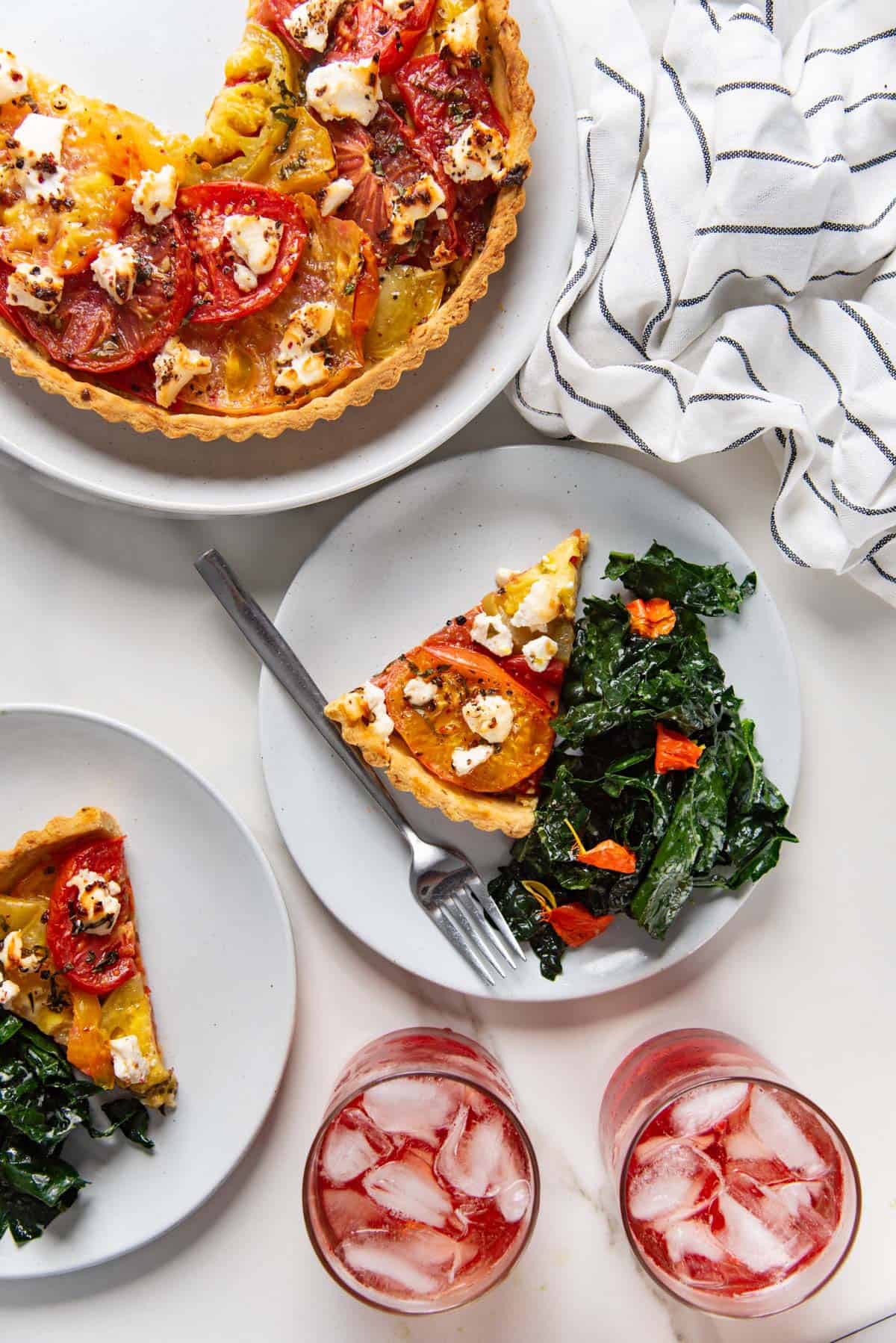 Overhead view of a fresh tomato tart with a slice cut out and served on a plate with a side salad.