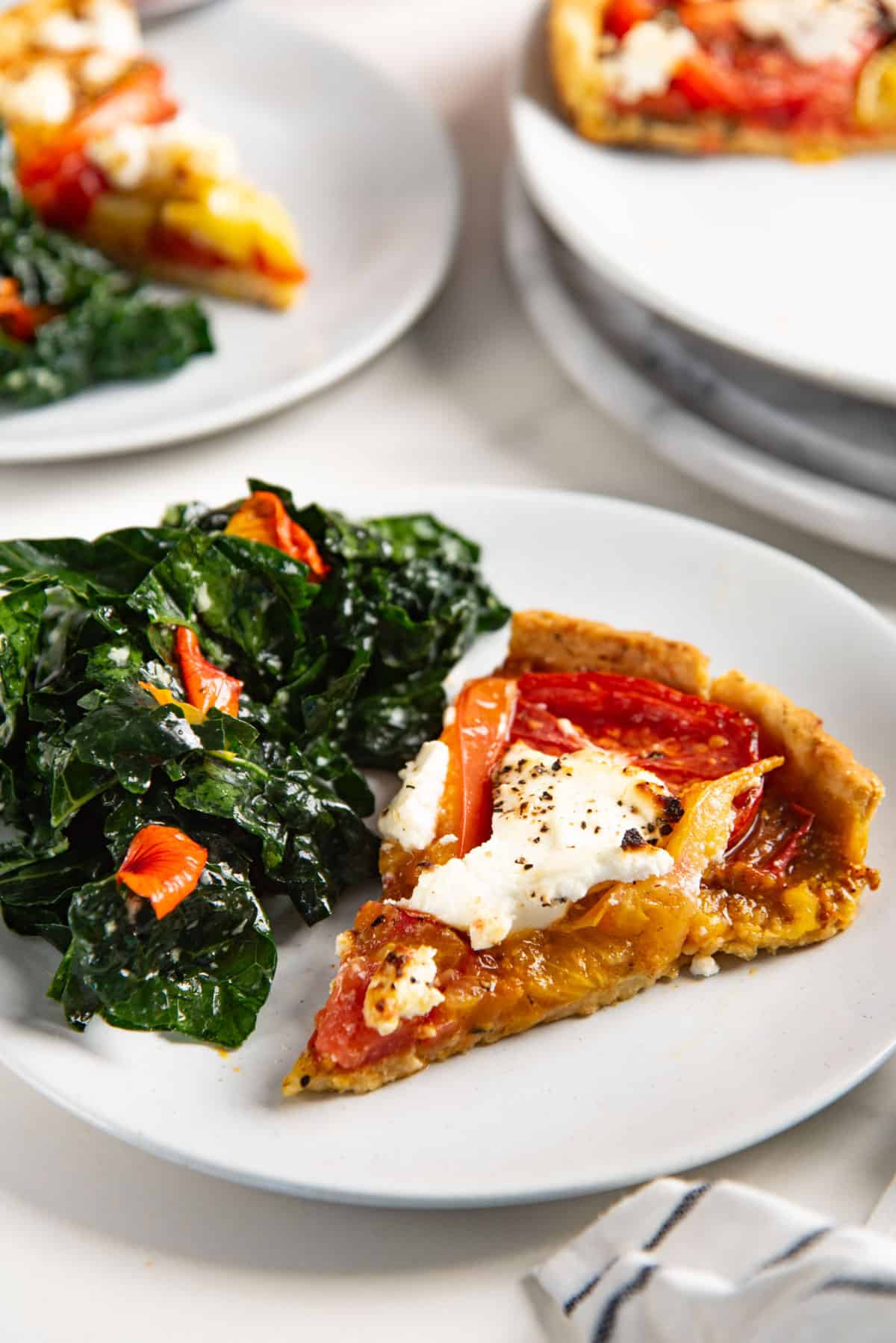 Close up of a tomato tart slice showing the caramelized goat cheese and feta cheese and tomato slices, and the kale salad.